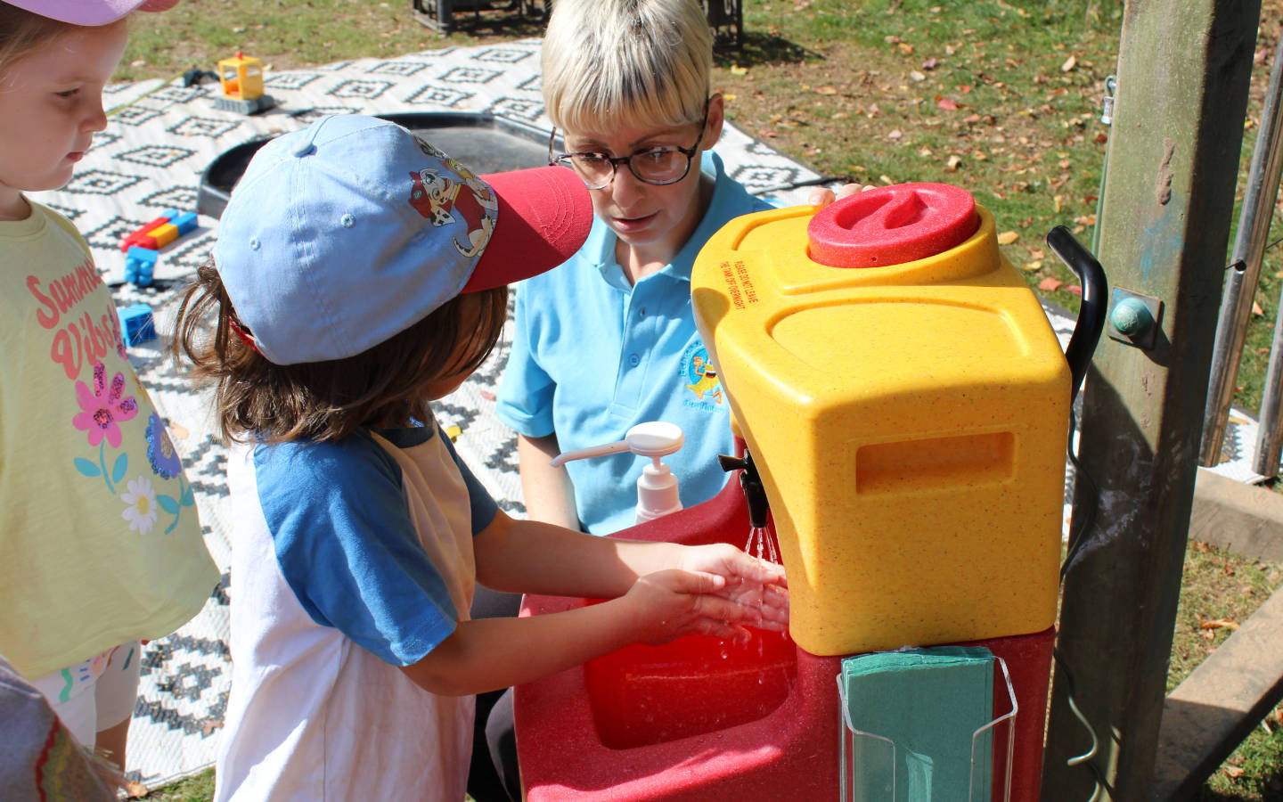 A boy being taught to wash his hands during outdoor play